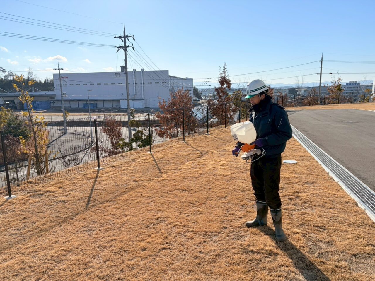 物流施設法面で発芽抑制剤を散布する植木屋スタッフ
